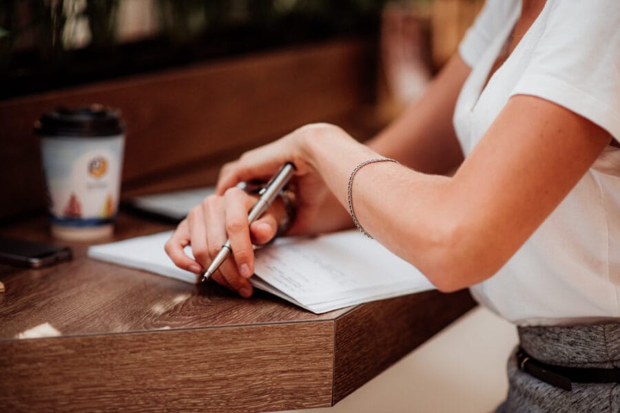 focus hands of a young woman as she is writing latter and notepad or something on a wooden table t20 gLJxk8 2